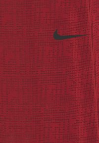 Czerwona koszulka sportowa z teksturowanym wzorem, z czarnym logo Nike na górnej lewej stronie. Materiał jest gładki, lekki i oddychający.