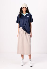 Marineblå kortärmad polo med ljusblå krage, avslappnad passform. Matchad med en beige midikjol. Modellen har på sig vita skor och en ljus keps.