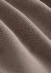 Jemná, strukturovaná tkanina v tlumené taupe barvě, s jemnými záhyby a tkaným vzorem, zdůrazňující její hladký povrch a hloubku.