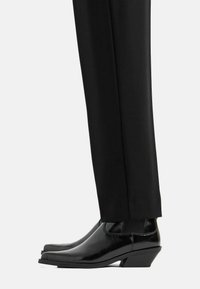 Stivaletti neri in pelle con un design elegante, dotati di pannelli laterali elasticizzati e un tacco piccolo, abbinati a pantaloni neri su misura.