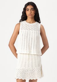 Robe tricotée blanche à design sans manches, avec une texture en dentelle à motifs, un bas superposé et un ourlet festonné.