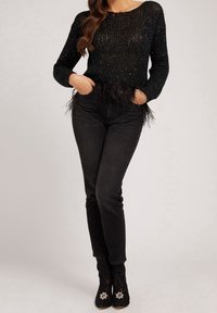 Czarny dzianinowy sweter z brokatem, ozdobiony piórami na dole. Połączony z czarnymi, dopasowanymi dżinsami i czarnymi botkami na wysokim obcasie.