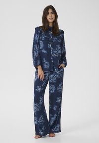 Mörkblå blommig pyjamasuppsättning med knapp-up topp och rynkad halsringning samt matchande vida byxor. Materialet verkar mjukt med en lätt lyster.