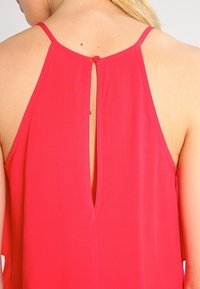 Top sin mangas en fucsia con un corte en forma de llave en la espalda, que presenta tirantes finos y una textura suave y fluida. Acabado con un pequeño botón.