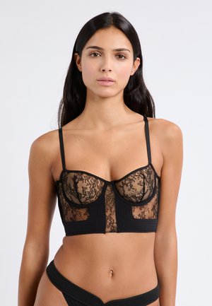 Schwarzer Spitzen-Bralette mit durchsichtigen Einsätzen und strukturierten Körbchen mit Rippendetails. Dünne, verstellbare Träger und eine gekürzte Silhouette.