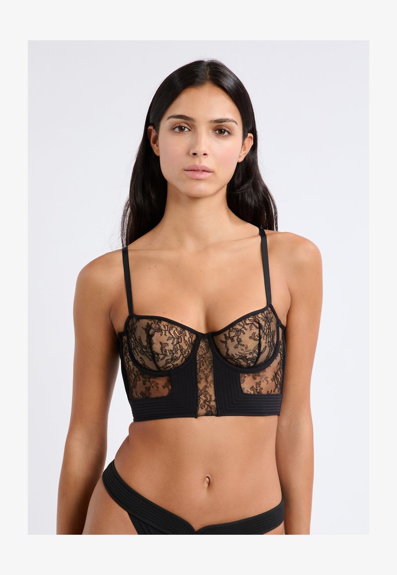 Zwarte kanten bralette met doorschijnende panelen en gestructureerde cups met geribbeld detail. Dunne verstelbare bandjes en een cropped silhouet.