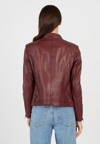 Bordeaux leren jack met gestructureerde schouderaccenten, een aansluitend ontwerp en ritssluitingen bij de mouwen, gecombineerd met lichtblauwe denim jeans.