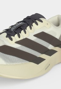 Gros plan sur une chaussure de course Adidas Adizero beige et noire avec des lacets noirs et un détail de semelle Lightstrike Pro.