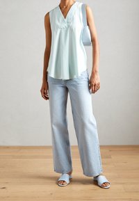 Blouse sans manches bleu clair avec un col en V, associée à un jean large bleu clair et des sandales assorties. Texture simple et lisse.