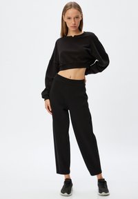 Sort cropped sweatshirt med lange ærmer, bukser med elastisk talje og sorte sneakers. Glat tekstur og minimalistisk design.