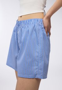 Pantaloni corti a righe blu e bianche con vita elasticizzata, tasche laterali e una vestibilità ampia, realizzati in tessuto leggero.