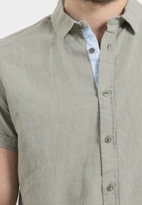 Chemise à manches courtes en lin vert doux avec une patte de boutonnage rayée bleu clair et des boutons verts, présentant une coupe décontractée et un design casual.