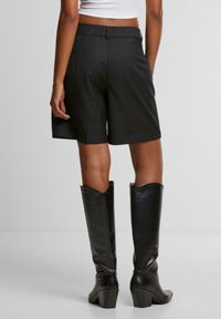 Černé ušité šortky s vysokým pasem a rovný střih. V kombinaci s černými koženými vysokými botami s blokovým podpatkem.