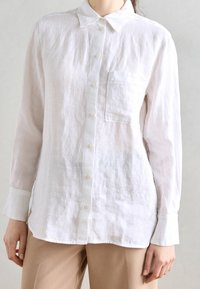 Wit linnen overhemden met knopen, een kraag, lange mouwen en een borstzak. Zachte textuur met een ontspannen pasvorm.