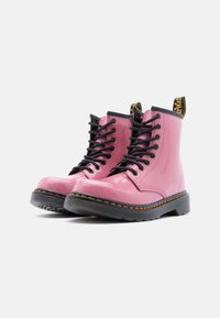 Ροζ μποτάκια αστραγάλου από δέρμα βινυλίου με μαύρα κορδόνια, στρογγυλεμένη μύτη και υφασμένο μαύρο καουτσούκ στη σόλα· διαθέτουν κίτρινη και μαύρη λουρίδα έλξης.