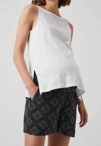 Bílý bezrukávový top z bavlny s volným střihem a postranními rozparky, spárovaný s černými šortkami s geometrickými vzory.