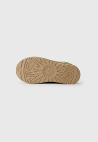 Suola della scarpa con un design testurizzato e a motivi in beige chiaro. Presenta un motivo a raggi di sole per garantire aderenza e durata.