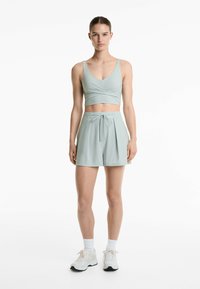 Světl zelený sportovní crop top s výstřihem do V a zkrouceným předním designem, spárovaný s odpovídajícími šortkami s vysokým pasem a tkaničkou.
