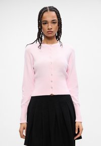 Ροζ ζακέτα πλεκτής ύφανσης με μακριά μανίκια και στρογγυλή λαιμόκοψη, που διαθέτει μία σειρά από κουμπιά μπροστά και κοντό στρίφωμα.