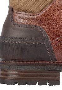 Bota de cuero marrón con parte superior de tela marrón texturizada, acentos suaves en marrón oscuro, suela de goma con detalles estriados y costuras reforzadas.