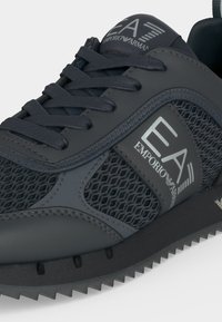 Baskets noires EA7 Emporio Armani avec panneaux en mesh, laçage sur l'avant et logo de la marque sur le côté et la languette.