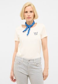 Camiseta de color crema con cuello redondo y mangas cortas, que presenta el texto bordado en azul marino "LES VACANCES" y pantalones ajustados a rayas.