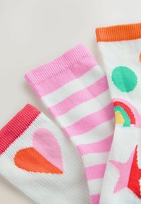 Chaussettes colorées avec un design rose uni, des rayures roses et blanches, et un motif à pois et cœurs blancs. Bords côtelés.