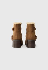 Brune ankelstøvler med en faux fur krave, sidelukninger og en struktureret mørk hæl, med en glat suede-lignende overflade.