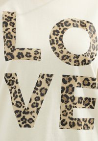 T-shirt color crema con grande testo "LOVE" in una stampa leopardata. Texture liscia con accenti di stampa animale scuri.