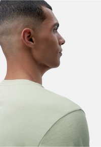 Világoszöld, rövid ujjú póló oldalról nézve, kerek nyakkivágással és puha tapintással, sima, minimalista dizájnnal.