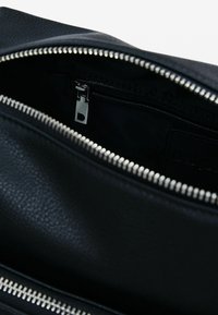 Zwarte leren tas interieur met zilveren rits. De voering is donker en er is een klein ritsvakje zichtbaar. Textuur van de buitenstof.