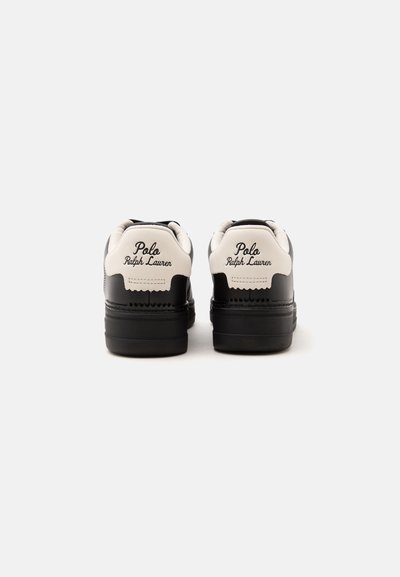Ασπρόμαυρα αθλητικά παπούτσια Polo Ralph Lauren, εμφανιζόμενα από πίσω με το κείμενο του ονόματος της μάρκας στην άσπρη περιοχή της φτέρνας.