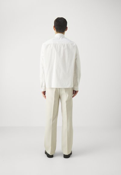 White button-up shirt with a boxy cut, long sleeves, and a smooth texture, paired with light beige, straight-leg trousers and black shoes.