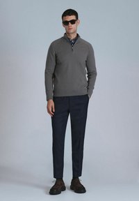 Grijze pullover met een ritskraag, marineblauwe op maat gemaakte broek en donkerbruine schoenen. Model draagt zwarte zonnebril. Glad textuur, getailleerd ontwerp.