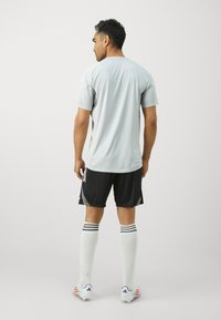 Lys grå atletisk t-skjorte med korte ermer, kombinert med svarte shorts. Hvite knestrømper med svarte striper og fotballsko med flerfargede aksenter.