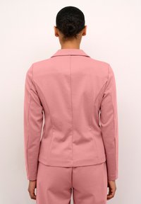 Roze sako s glatkom teksturom, prilagođenim dizajnom, klasičnim reverima i detaljima šavova. Pogled sa stražnje strane prikazuje duge rukave i oblikovani kroj.