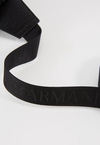 Černý textilní pásek s embosovaným logem "ARMANI", hladký povrch s matným finish, připojený k texturované části z černé kůže.