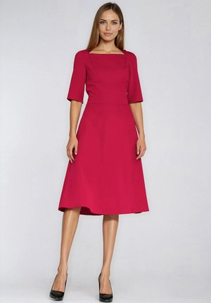 Midi sukienka w kolorze fuksji z kwadratowym dekoltem, krótkimi rękawami i rozkloszowanym dołem, wykonana z gładkiego materiału; dopełniona czarnymi szpilkami.