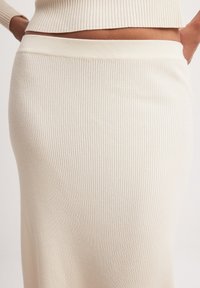 Strickrock in Creme mit vertikaler Rippstruktur, ausgestattet mit einem hohen Bund. Der Stoff wirkt weich und elastisch. Einfaches und figurbetontes Design.