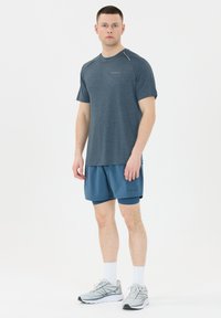 Mansk sportklädsel bestående av en mörkblå kortärmad skjorta och matchande shorts. Ljusgrå sneakers med vita detaljer och strumpor.