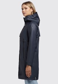 Chaqueta impermeable de color navy con capucha, cremallera de longitud completa, bolsillos laterales y detalles a presión en las mangas. Textura suave y brillante.