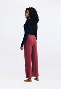 Aansluitend zwart langemouwen top gecombineerd met losse, high-waisted, donkerrode broek; soepel materiaal en elastische tailleband zichtbaar.