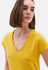 T-shirt jaune à manches courtes avec un décolleté en V, fabriqué en tissu texturé, présentant une coupe décontractée et des détails de couture subtils.