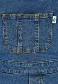 Denim fabric pocket with blue color, golden stitching, and a small green label featuring a leaf in the upper corner.