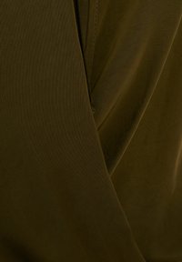 Tessuto verde oliva con una texture liscia, caratterizzato da strati drappeggiati e una leggera lucentezza. Le cuciture evidenziate aggiungono un dettaglio raffinato.