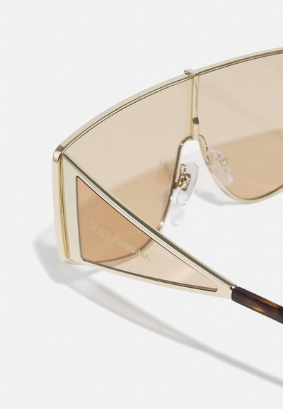 Ochelari de soare cu un cadru geometric de ton auriu, lentile brune cu gradient și tampoane pentru nas clare distinctive; au branding pe lateral.