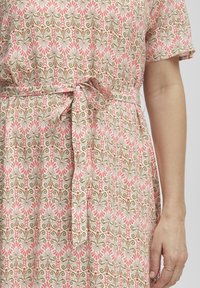 Robe à motifs floraux avec un design rose et vert, fabriquée en tissu léger, dotée d'une taille nouée et de manches courtes.