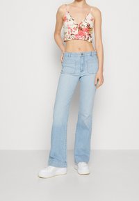 Kukallinen lyhythihainen crop-top, jossa on ohuet hihnat, yhdistettynä vaaleansinisiin leveälahkeisiin farkkuihin ja valkoisiin tennareihin. Asusteessa on rento istuvuus ja epämuodollinen tyyli.