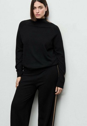 Sudadera negra de punto y pantalones a juego con cuello alto, con textura sólida y franjas laterales contrastantes en color camel.