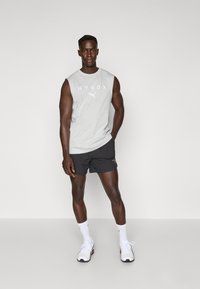 Grå ermeløs T-skjorte med "HYROX" trykk og svarte treningsshorts. Hvite joggesko og sokker fullfører den sporty stilen. Enkel design, minimalistisk stil.